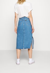 Vaaleansininen denimmidihame, jossa on takakaitale, kaksi takataskua ja korkea vyötärö. Yhdistetty valkoisiin korkeavartisiin lenkkareihin.