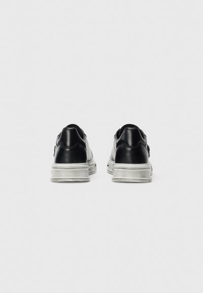 Pair of black leather sneakers with white rubber soles viewed from the back on a plain white background.