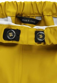 Gelbe wasserdichte Jacke mit elastischem Bund, versehen mit schwarzen Knopf- und Riemenschließen sowie einem weißen Innenfutter. Markenlabel sichtbar.