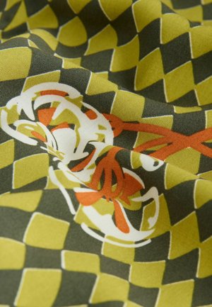 Textil med ett grönt och gult rutmönster med blomsterdetaljer i vitt och orange, som visar en slät, vävd struktur.