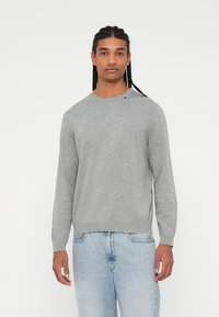 Maglione grigio chiaro lavorato a maglia con scollatura rotonda e polsini a coste, abbinato a jeans in denim blu chiaro. Nessun motivo o dettaglio visibile.