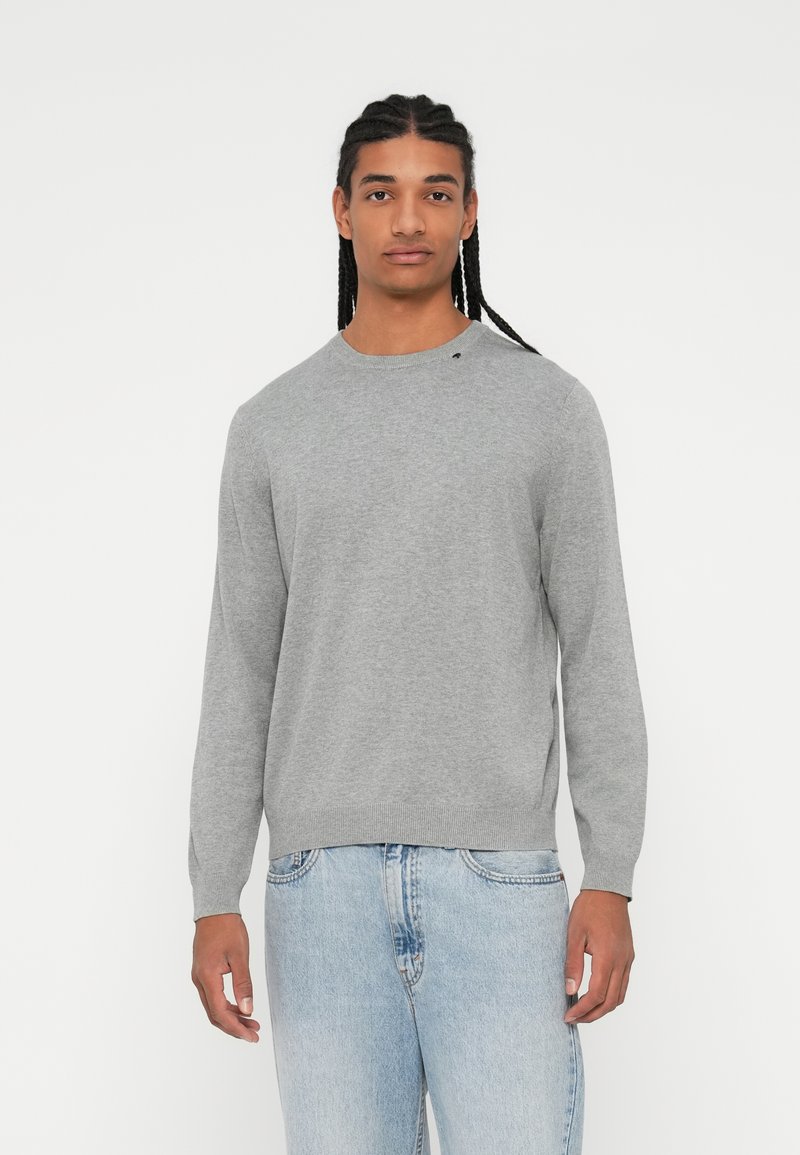Maglione grigio chiaro lavorato a maglia con scollatura rotonda e polsini a coste, abbinato a jeans in denim blu chiaro. Nessun motivo o dettaglio visibile.