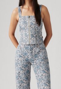 Blå denimtop med blommönster, dragkedja framtill och breda axelremmar, matchad med byxor i blommönstrad denim. Texturerad och åtsittande design.