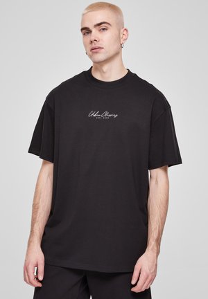 T-shirt in cotone nero con una vestibilità rilassata, caratterizzato da un logo bianco "Urban Classics" sul petto. Maniche corte e scollatura rotonda.