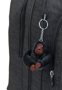 Ullig svart gorillanyckelring fäst vid en mörk tygryggsäck, med en metallklämma och rosa ansiktsdetaljer. Texturerad design är framträdande.