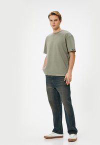 Camiseta de algodón verde de gran tamaño con escote redondo y mangas cortas, combinada con jeans de pierna recta azul oscuro y zapatillas blancas.