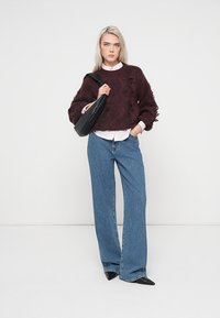 Maglione bordeaux con texture e maniche a sbuffo, abbinato a jeans a gamba larga azzurri. Una borsa nera completa il look.