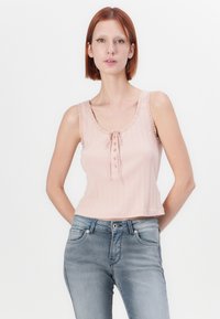 Top corto sin mangas de color rosa claro con textura acanalada, bordes en forma de ondas y cierre delantero con botones. Combinado con jeans azul desteñido.