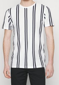 Vit t-shirt med kort ärm som har vertikala marinblå ränder, rundad halsringning och avslappnad passform. Tillverkad av lätt, texturerad tyg.