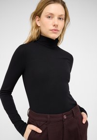 Czarny prążkowany top z długim rękawem i golfem, zestawiony z dopasowanymi głęboko bordowymi spodniami z przodu zapinanymi na guzik i z bocznymi kieszeniami.