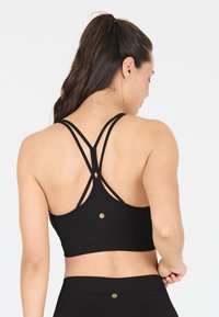 Soutien-gorge de sport noir avec une texture côtelée, un design dos nageur avec des bretelles entrecroisées doubles, et un petit logo doré en accent au dos.