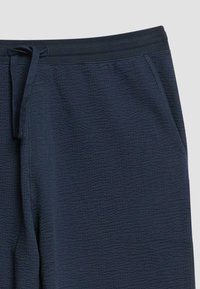Pantalon bleu marine texturé avec cordon de serrage et poches latérales, présenté de la taille au milieu de la cuisse sur un fond clair.