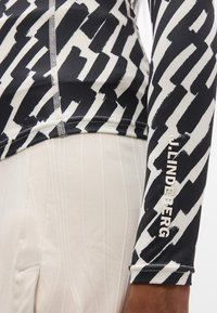 Μακρυμάνικη αθλητική μπλούζα με έντονο μαύρο και λευκό αφηρημένο σχέδιο, εφαρμοστή σχεδίαση και τυπωμένο λογότυπο στο μανίκι.