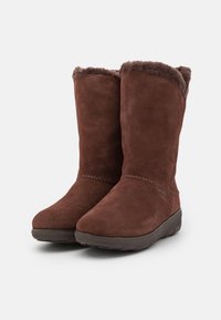 Bottes montantes en daim marron avec doublure douce en fausse fourrure, semelle plate en caoutchouc et coutures décoratives le long de la couture.