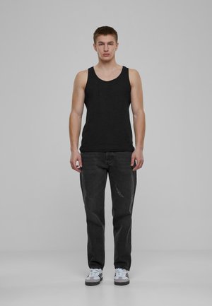 Sort tanktop med rund halsudskæring, parret med slidte sorte jeans. Modellen står i hvide sneakers mod en plain grå baggrund.