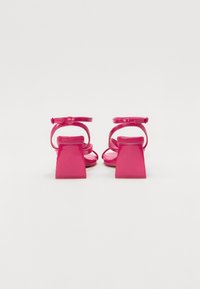 Rosa høyhælte sandaler med bred firkantet hæl, tynne ankelstropper og åpen tå-design, med en blank lakkfinish.