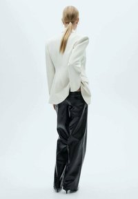 Witte op maat gemaakte blazer met gestructureerde schouders, gecombineerd met high-waisted zwarte neplederen broeken met een krokodillenpatroon.