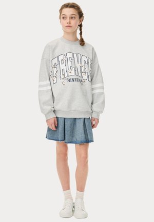 Szara bluza z nadrukiem "FRENCH RIVIERA" i kwiatowymi akcentami, w połączeniu z dżinsową spódnicą. Białe sneakersy i jasne skarpetki dopełniają stylizację.