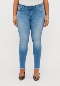 Skinny blue jeans made of denim, featuring a mid-rise waist, five-pocket design, and slight frayed hem. Worn with leopard-print heels.