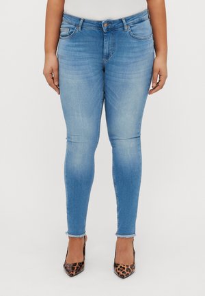 Skinny blue jeans made of denim, featuring a mid-rise waist, five-pocket design, and slight frayed hem. Worn with leopard-print heels.
