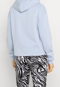 Sweat à capuche bleu clair avec un design court, associé à un pantalon à motif tourbillonnant noir et blanc. La texture douce du tissu est visible.