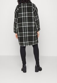 Zwarte en groene geruite jas met een relaxte pasvorm, lange mouwen en een zachte textuur, gecombineerd met zwarte leggings en chunky haklaarzen.