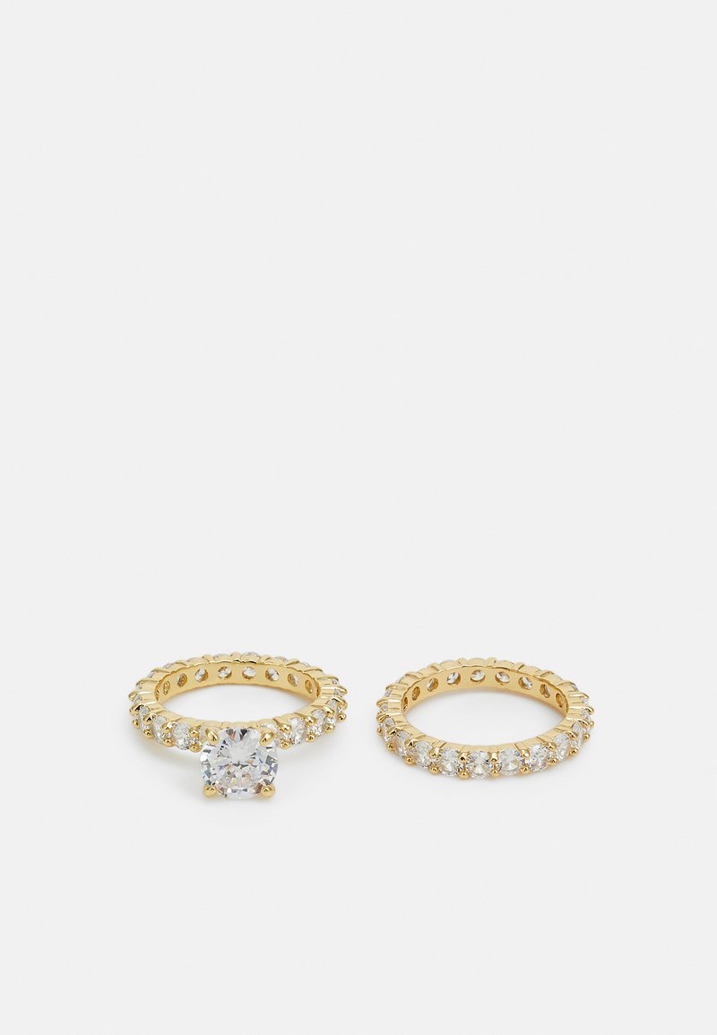 Dos anillos de oro. Uno presenta una piedra central clara, rodeada de piedras claras más pequeñas. El otro tiene una banda completa de piedras claras.