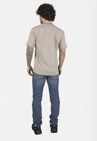 T-shirt in cotone beige con maniche corte, vestibilità comoda e colletto rotondo. Abbinato a jeans in denim blu e sneakers nere.