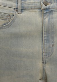 Jeans en denim bleu clair présentant un design classique à cinq poches, des coutures visibles, une fermeture boutonnée et une finition délavée avec des textures variées.
