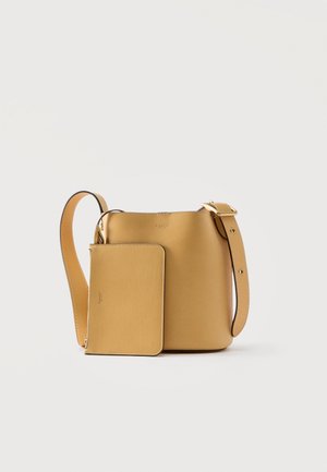 Sac seau Coach en cuir tan avec pochette assortie détachable, bandoulière ajustable et embossage de logo subtil sur fond blanc.