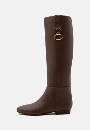 Botte haute en cuir marron avec semelle plate et détail d'une boucle circulaire dorée sur le côté supérieur.
