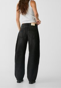 Czarne dżinsowe spodnie o szerokim kroju z wysokim stanem, z dwoma tylnymi kieszeniami, naszywką z tyłu i luźnym krojem w okolicy kostek.