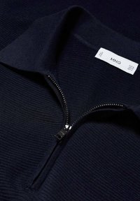 Pull en maille bleu marine foncé avec une demi-fermeture éclair et un col replié, montrant une étiquette de marque blanche à l'intérieur.