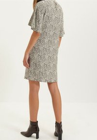 Vestido de manga corta en una tela color crema con un patrón salpicado en negro, corte hasta la rodilla, con un escote en la parte posterior y combinado con botas hasta el tobillo.