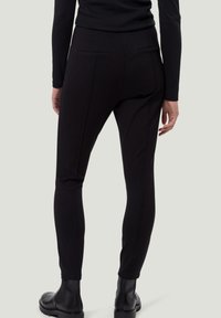 Pantalon noir longueur cheville en tissu extensible. Comprend deux poches arrière, une coupe slim et des lignes épurées. Porté avec des bottines noires.