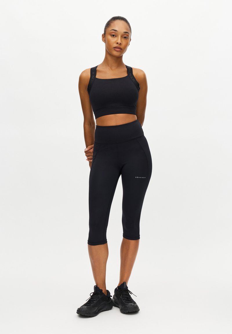 Svart sportcroptopp med breda band och matchande höga caprileggings. Båda plaggen har en slät, åtsittande design.