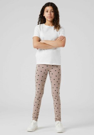 T-shirt bianco a maniche corte abbinato a leggings beige con un motivo a cuori neri, completato da sneaker bianche.
