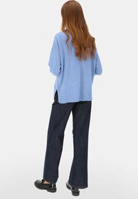 Jasnoniebieski sweter z dzianiny z prążkowanym ściągaczem, noszony na szerokich, ciemnoniebieskich dżinsach z szerokimi nogawkami i czarnych butach na platformie, o luźnym kroju i bocznych rozcięciach.
