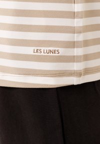 Camiseta de algodón a rayas beige y blanca con el logo bordado "LES LUNES" cerca del dobladillo, que presenta una textura suave y un diseño sencillo.