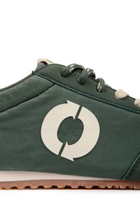 Baskets vertes avec logo de flèche circulaire blanc, semelle en caoutchouc texturée et lacets vert foncé avec accents blancs sur fond blanc.