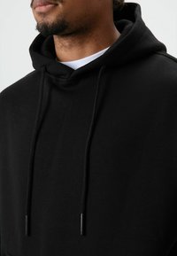 Zwarte katoenen hoodie met trekkoorden, met een losse pasvorm en een zachte textuur; inclusief een gelaagd wit shirt eronder.