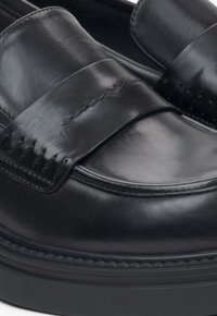 Zwarte leren instappers met een gladde afwerking, voorzien van een brede band en gedetailleerde stiksels langs de randen. Slanke, ronde vorm.