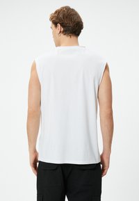 Vit ärmlös t-shirt i bomull, med rund halsringning och avslappnad passform. Baksidan visar en slät textur och minimalistisk design.