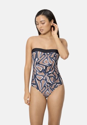 Mujer con cabello largo y oscuro que lleva un traje de baño de una pieza sin tirantes con un patrón geométrico abstracto en tonos negro, marrón y azul.