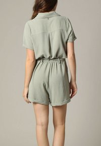 Korte, olijfgroene playsuit van gestructureerde stof. Heeft een kraag, opgerolde mouwen, een elastische taille en een subtiele plooi aan de achterkant.