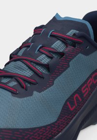 Chaussure de sport bleu et marine avec des lacets accentués de rouge et le logo "LA SPORT" sur le côté, mettant en valeur un matériau en mesh respirant et des coutures détaillées.