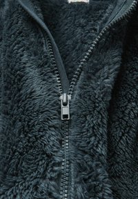 Bluza polarowa w ciemnoszarym kolorze z miękkim, teksturowanym materiałem. Posiada zamek błyskawiczny na całej długości z gładkim uchwytem i podszytymi brzegami.