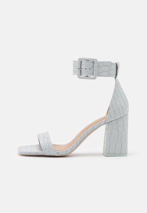Lysegrå højhælet sandal med blokhæl, ankelrem og spænde samt en enkelt frontrem med krokodillemønster.
