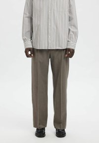 Črtasta srajca s srajčnimi gumbi v svetlo sivi in beli barvi, kombinirana z širokimi svetlo sivimi hlačami; teksturirana tkanina, sprednji žep na srajci, črni čevlji.