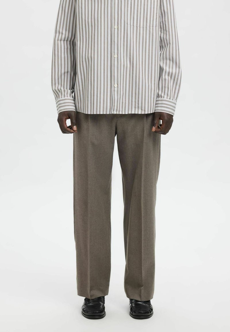 Črtasta srajca s srajčnimi gumbi v svetlo sivi in beli barvi, kombinirana z širokimi svetlo sivimi hlačami; teksturirana tkanina, sprednji žep na srajci, črni čevlji.